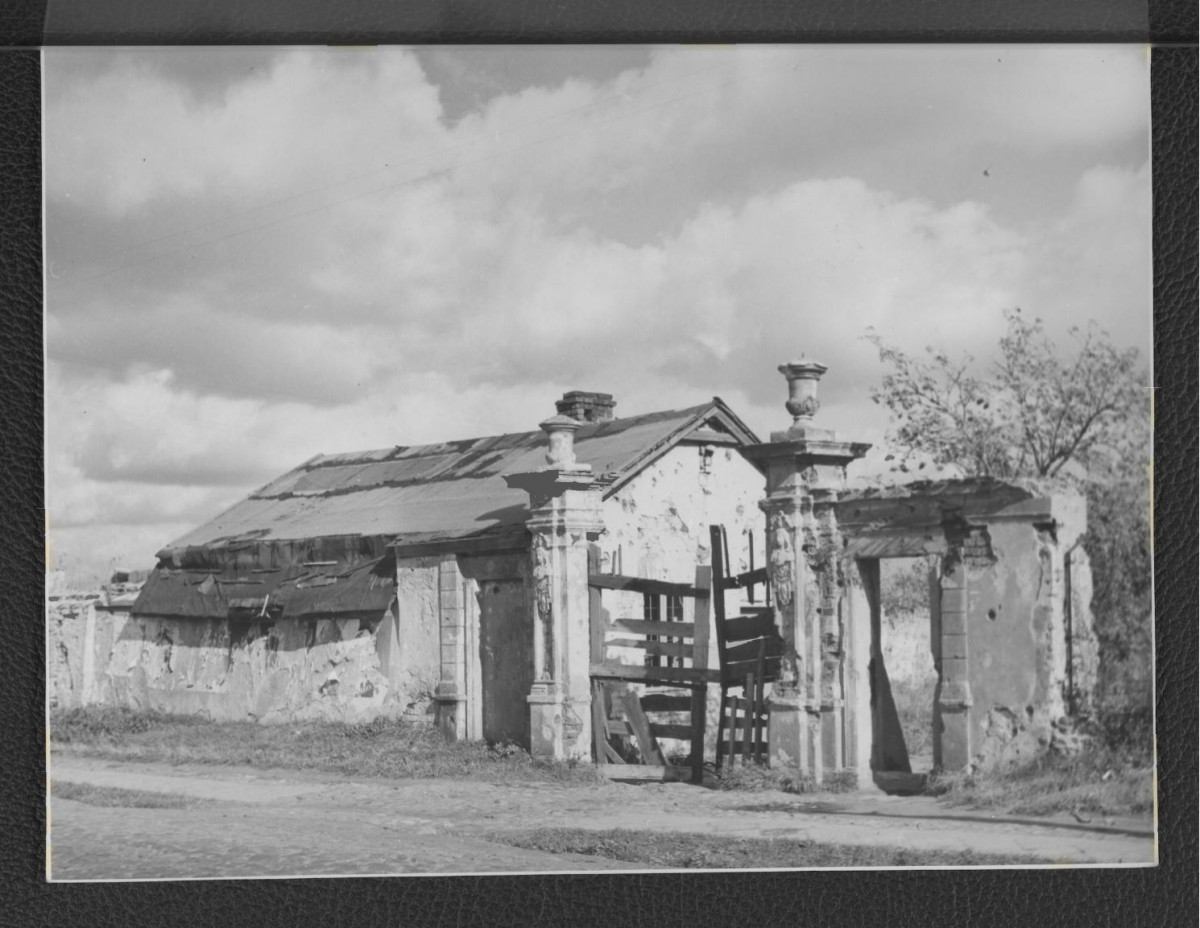 fotografia czarno-biała przedstawiająca fragment zniszczonych zabudowań dworskich, w tym zdobionego reliefami ogrodzenia, skan 1
