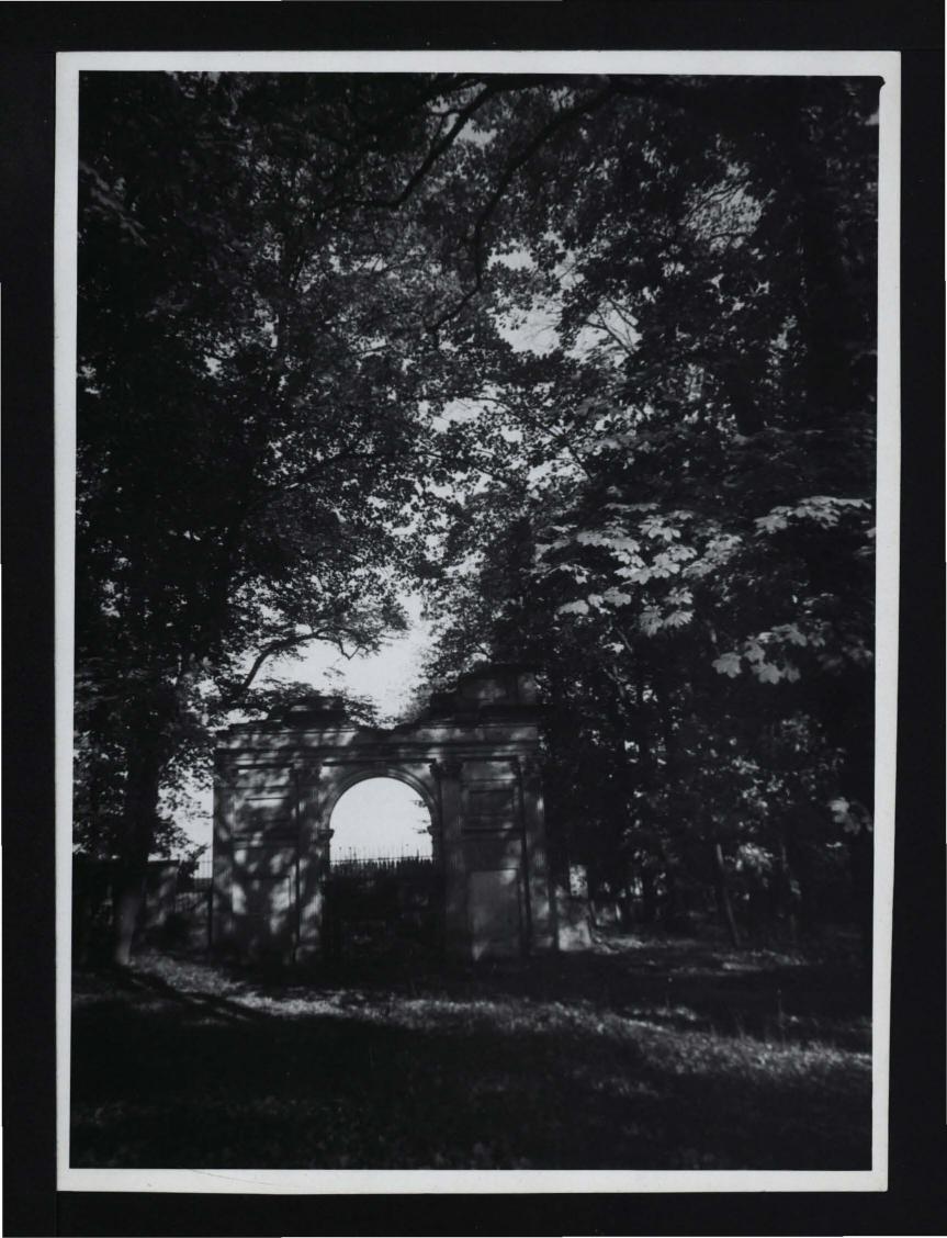 fotografia czarno-biała przedstawiająca łuk (tzw. Brama Rzymska) w ramach ogrodzenia miejscowego parku, skan 1