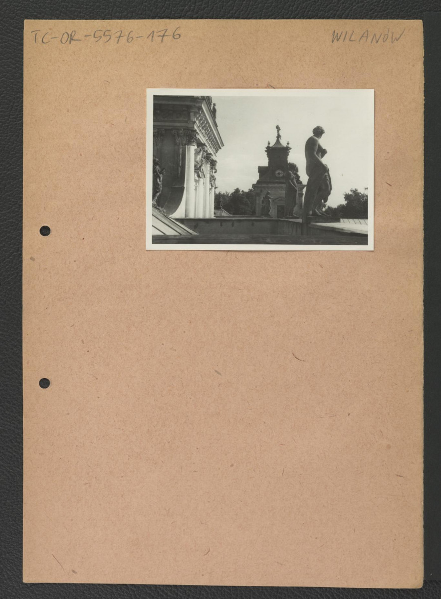 fotografia czarno-biała przedstawiająca rzeźby wieńczącę gzyms pałacu na tle południowej wieży zegarowej                                                                            , skan 1