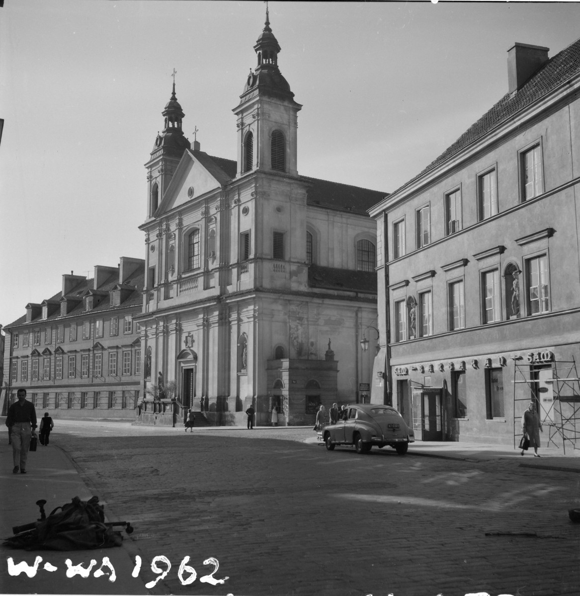 Kościół św. Ducha. Odbudowa. Fasadę ujętą osiowo, zamykającą widok wznoszącej się ku górze brukowanej jezdni. Świątynia ma dwukondygnacyjną fasadę, uporządkowaną pionowymi podziałami pilastrów i zwieńczoną trójkątnym przyczółkiem. Po bokach stoją dwie smukłe, odbudowane wieże, nakryte hełmami z latarniami i krzyżami. , skan 1
