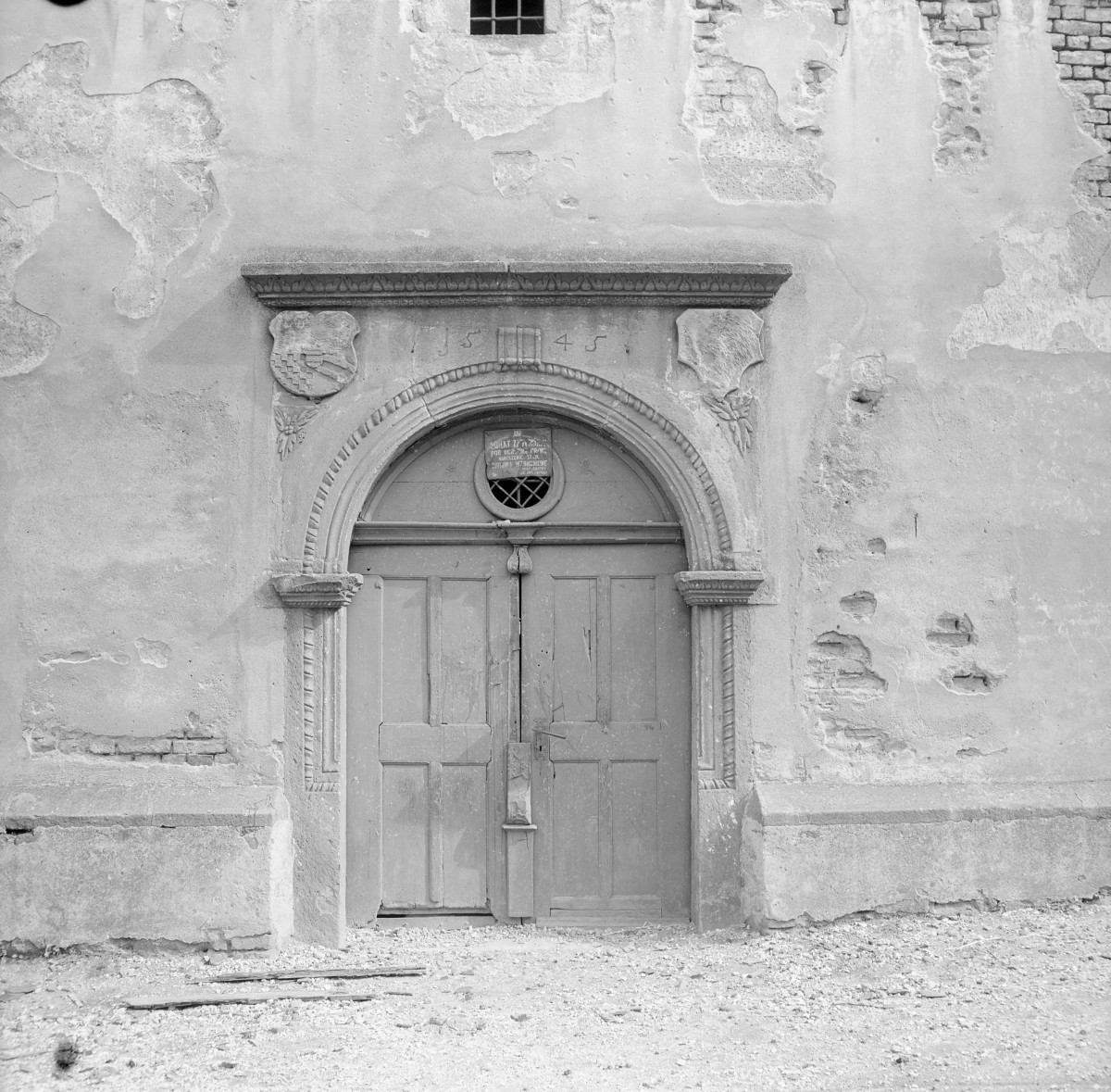 Kościół św. Krzysztofa. Portal zachodni kamienny, renesansowy w formie, osadzony w surowej, tynkowanej elewacji wieży. Otwór ujęty jest profilowaną archiwoltą z dekoracyjnym, wałkowym obramieniem. Archiwolta wspiera się na dwóch prostych pilastrach o delikatnie zaznaczonych głowicach i bazach. Powyżej łuku biegnie poziomy gzyms z ornamentalnym fryzem o motywie roślinnym. Nad archiwoltą umieszczono datę „1545”, wskazującą na czas powstania portalu. Po obu stronach daty znajdują się płaskorzeźbione tarcze herbowe – obecnie silnie zatarte i trudne do jednoznacznej identyfikacji – podtrzymywane przez stylizowane motywy roślinne. W polu nad drzwiami znajduje się niewielki, okrągły otwór (okulus) z metalową kratą; wewnątrz widoczna jest tabliczka z napisem., skan 1