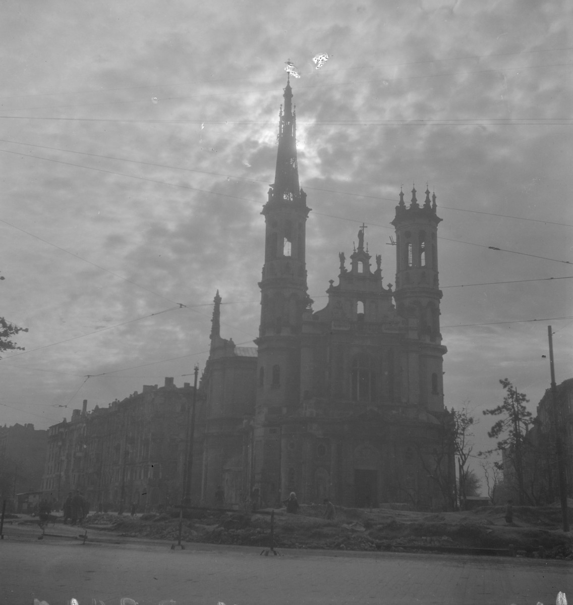 Kościół Najświętszego Zbawiciela. Zniszczenia. Fasada jest dwuwieżowa, przy czym szczególnie silnie zaznacza się jedna z wież, zwieńczona bardzo smukłym, strzelistym hełmem. Wieże zostały ukształtowane wielokondygnacyjnie, z wyraźnie wydzielonymi strefami i prześwitami okiennymi w partiach górnych. , skan 1