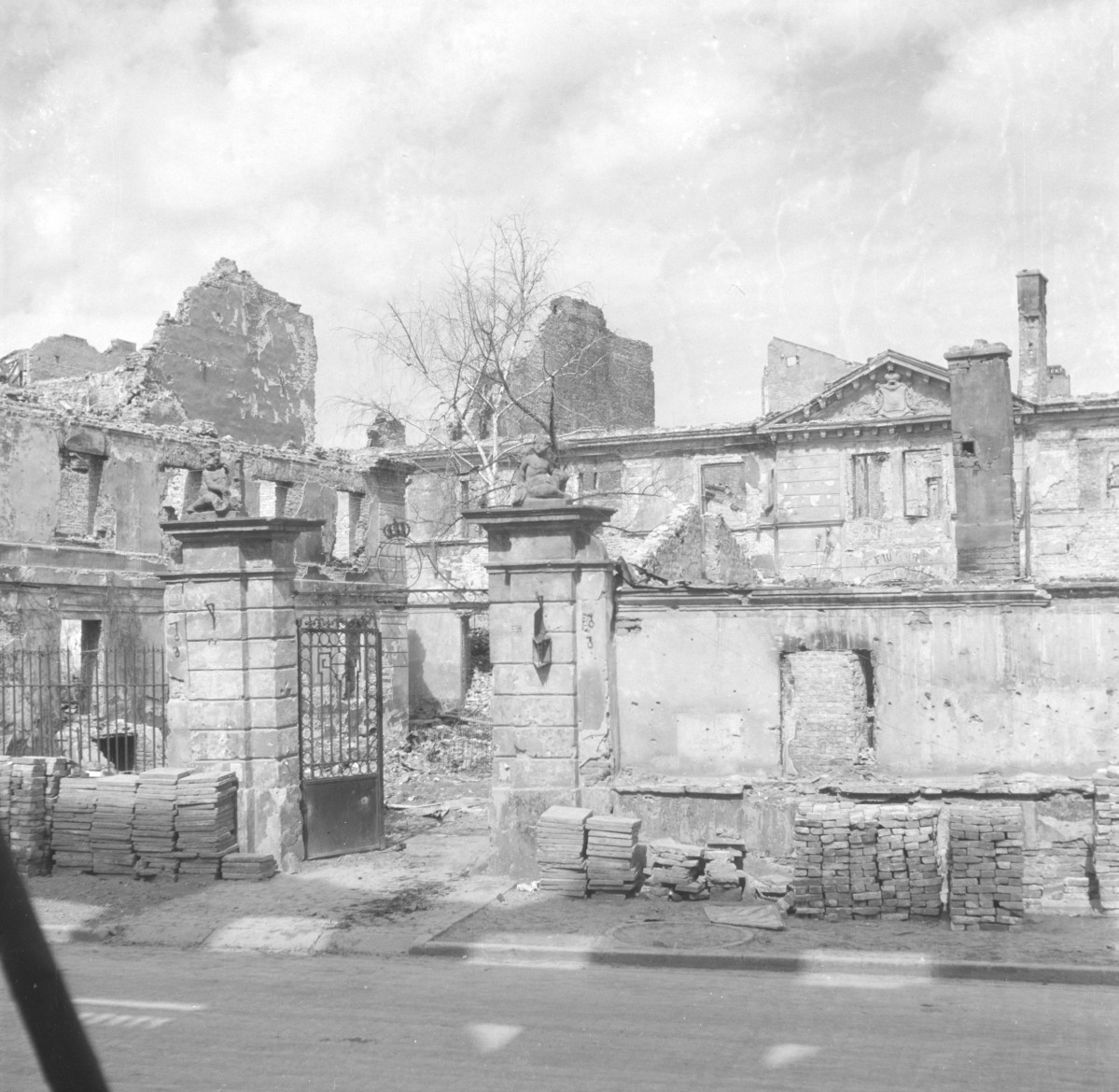 Zniszczony pałac Lubomirskich - Widok od strony ul. Długiej. Brama wjazdowa z rzeźbami na szczycie. Na uprzątniętym chodniku poustawiane cegły i płyty, gotowe do odbudowy budynku., skan 1