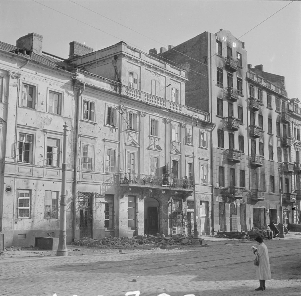 Kamienica Jacobsona. Elewacja frontowa i widok ogólny. W centralnej osi przejazd bramny. Nad przejazdem mały balkon z balustradą wsparty na konsolach. Między oknami rozmieszczone pilastry, które porządkują rytm fasady. Okna z naczółkami trójkątnymi oraz jeden przerywany segmentowy. Na chodniku przed budynkiem sterta gruzu. , skan 1