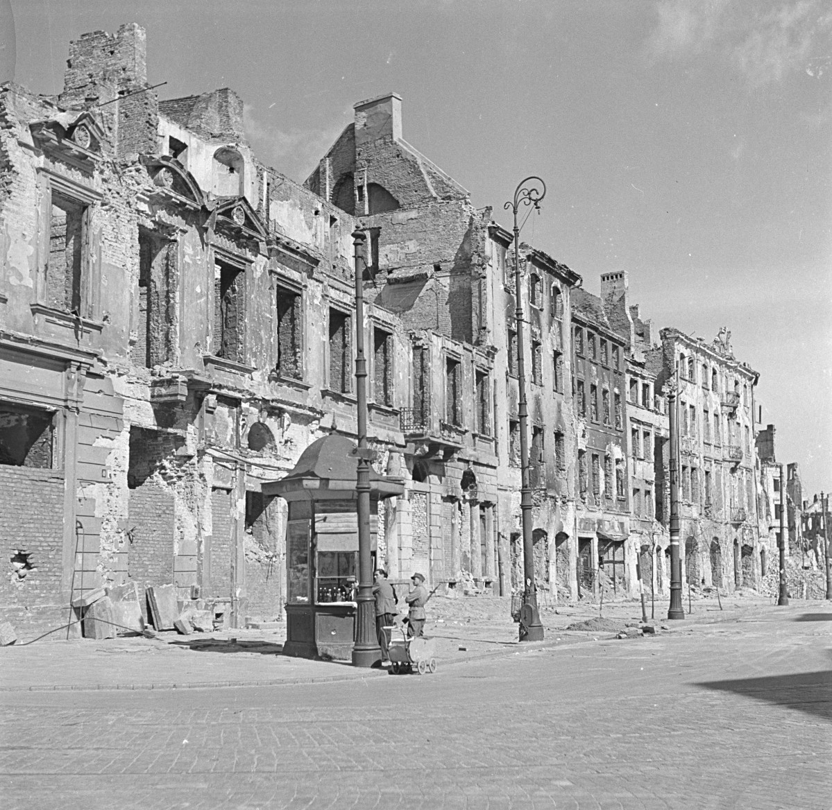 Zniszczone kamienice w pobliżu ul. Miodowej. Na pierwszym planie kiosk z napojami i klienci. , skan 1