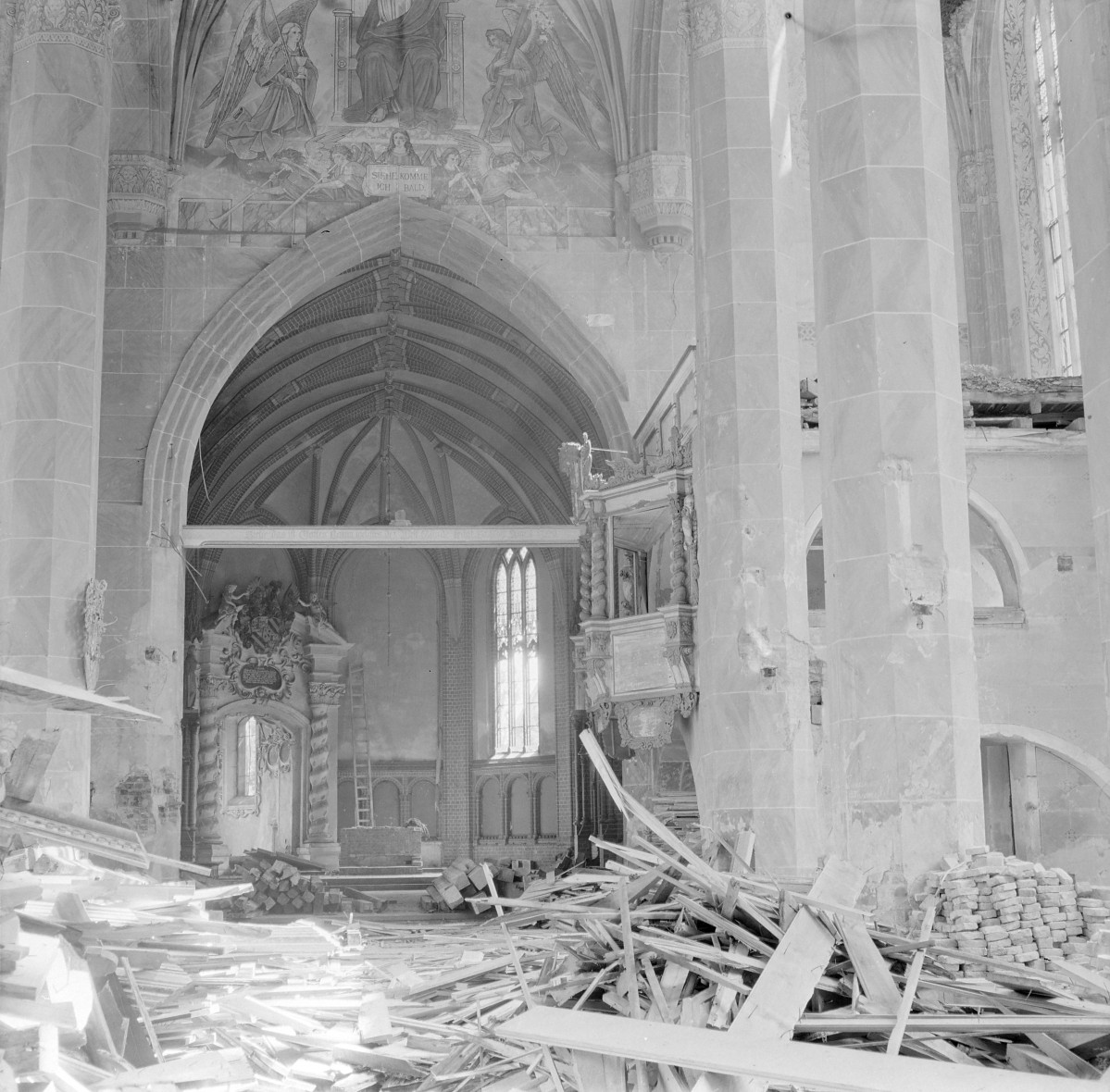 Kościół pw. WNMP. Wnętrze. Nawę oraz przejście w kierunku prezbiterium. Wysokie, smukłe arkady o ostrołukowych zamknięciach, oparte na masywnych filarach o gładkich, wielobocznych trzonach. Ponad arkadą rozpięte jest sklepienie żebrowe – żebra tworzą rytmiczny, wyraźnie zaznaczony układ konstrukcyjny, podkreślający wertykalizm przestrzeni. W głębi widoczne są wysokie, ostrołukowe okna z maswerkami, doświetlające prezbiterium. Ściany w górnych partiach pokryte są polichromią figuralną. Nad arkadą widnieje monumentalne przedstawienie Chrystusa w majestacie w otoczeniu aniołów, wpisane w architektoniczne ramy pola malarskiego. Dekoracja ta wskazuje na historyzującą, zapewne XIX-wieczną lub wczesno-XX-wieczną aranżację wnętrza. Po prawej stronie widoczna jest bogato dekorowana ambona o formach barokowych, z profilowanym koszem i ornamentalnym baldachimem. , skan 1