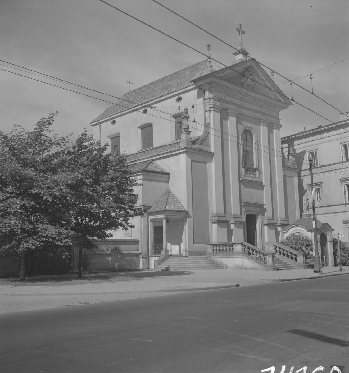 Kościół Przemienienia Pańskiego. Odbudowa. Centralna część fasady akcentuje wysoki otwór okienny o zamknięciu łukowym, umieszczony ponad głównym wejściem. Portal wejściowy jest prosty, ale wyraźnie osadzony w osi kompozycji. Bryła kościoła jest wydłużona i salowa, z prostym korpusem nawowym rozciągającym się za fasadą. Po bokach widoczne są niższe aneksy lub kaplice, również opracowane w uproszczonych formach klasycyzujących, z własnymi małymi naczółkami. Elewacje boczne są znacznie spokojniejsze od frontu. , skan 1
