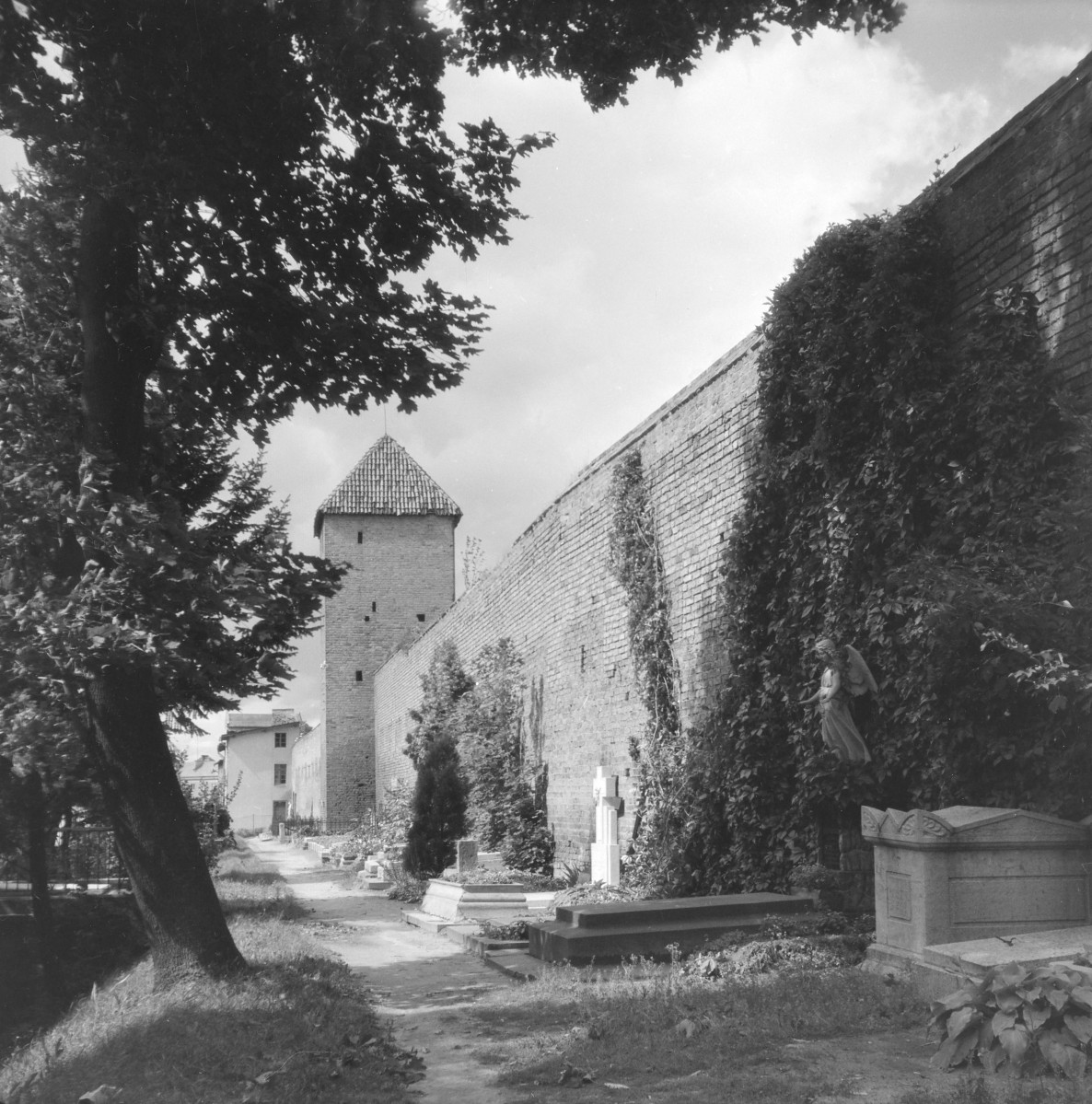 Mury miejskie z widoczną Basztą Prochową. Na pierwszym planie widzoczne nagrobki., skan 1