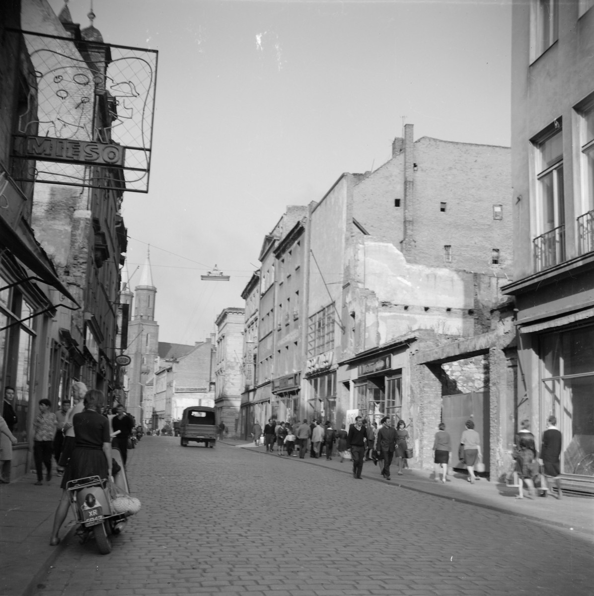 Zabudowa miejska. Oś widokowa w kierunku rynku. W oddali widoczne wieże kościoła Mariackiego. Po lewej stronie widoczny neon sklepu mięsnego., skan 1