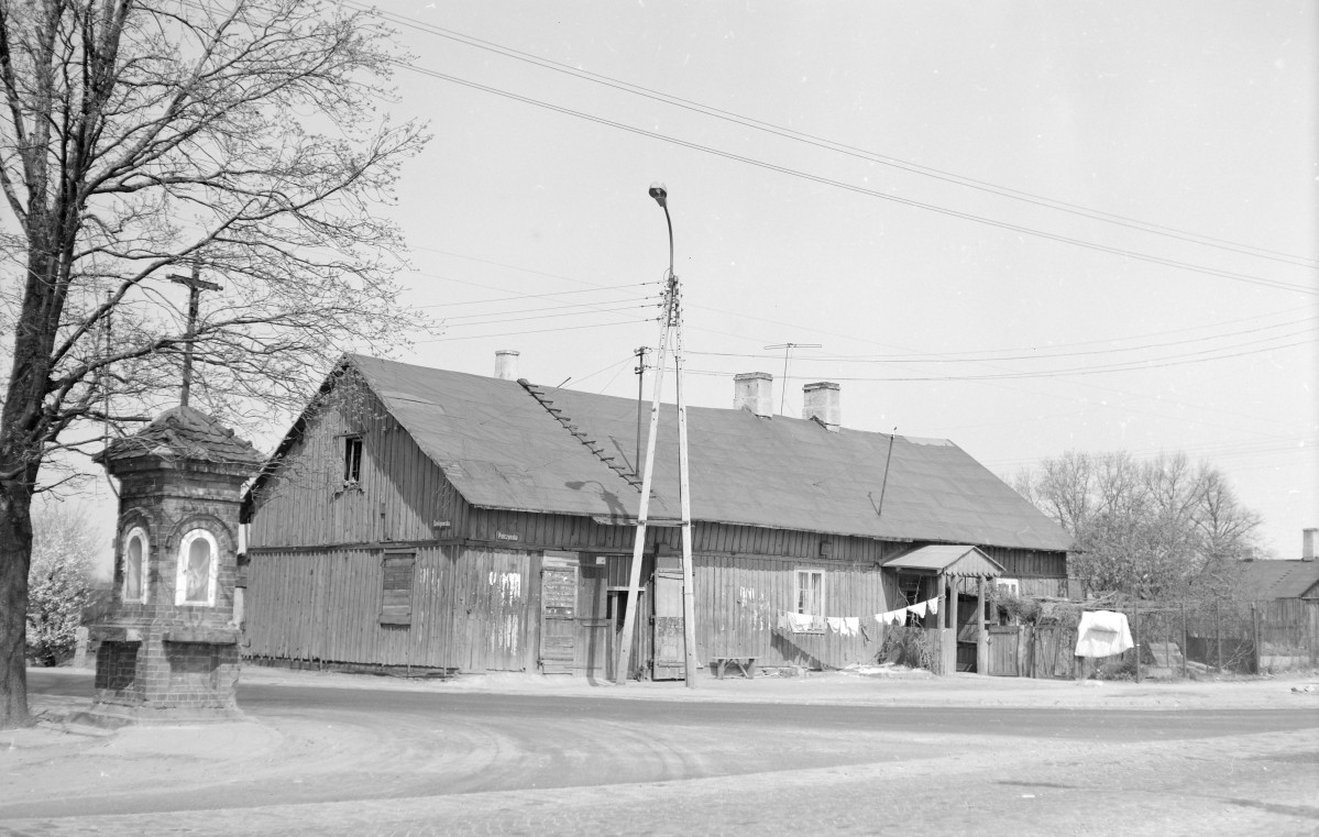 Drewniany dom - zabudowa miejska. Szalowany deskami. dach dwuspadowy. Drewniany ganek. Przed domem kapliczka przydrożna., skan 1