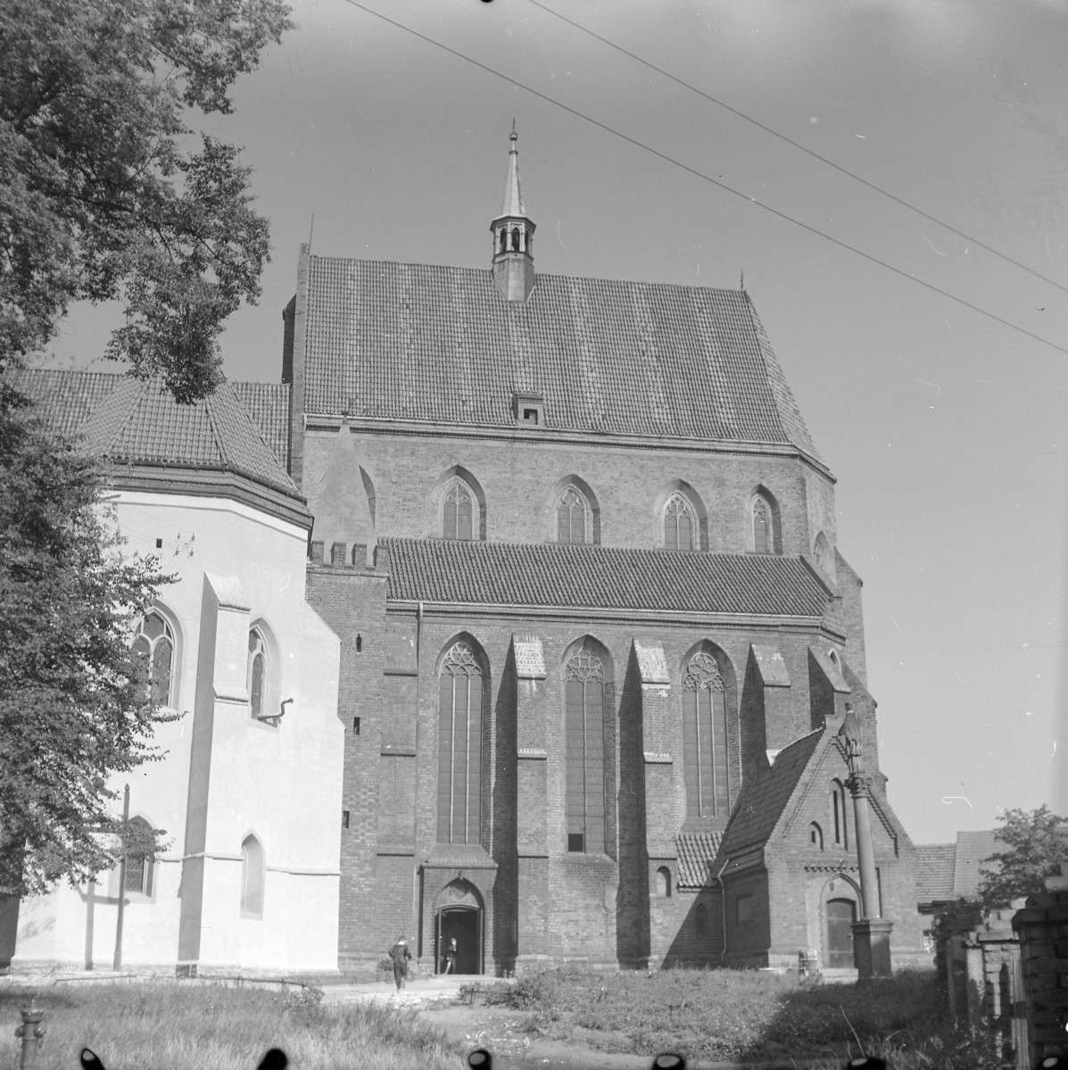 Bazylika św. Jerzego. Budynek ma masywną, zwartą bryłę i wysokie, dwuspadowe dachy pokryte dachówką ceramiczną. Nad główną częścią wznosi się smukła sygnaturka (mała wieżyczka) zakończona ostrosłupowym hełmem. Elewacje wykonane są z czerwonej cegły, co podkreśla gotycki charakter budowli. Najbardziej charakterystycznym elementem są wysokie, ostrołukowe okna z maswerkami, rozmieszczone pomiędzy przyporami wzmacniającymi ściany. Pionowe linie przypór oraz strzeliste okna nadają świątyni smukłości i podkreślają jej wertykalizm – typową cechę gotyku. Do głównej bryły przylegają niższe przybudówki – kaplice oraz aneksy o osobnych dachach. Widoczne jest również wejście główne z ostrołukowym portalem., skan 1