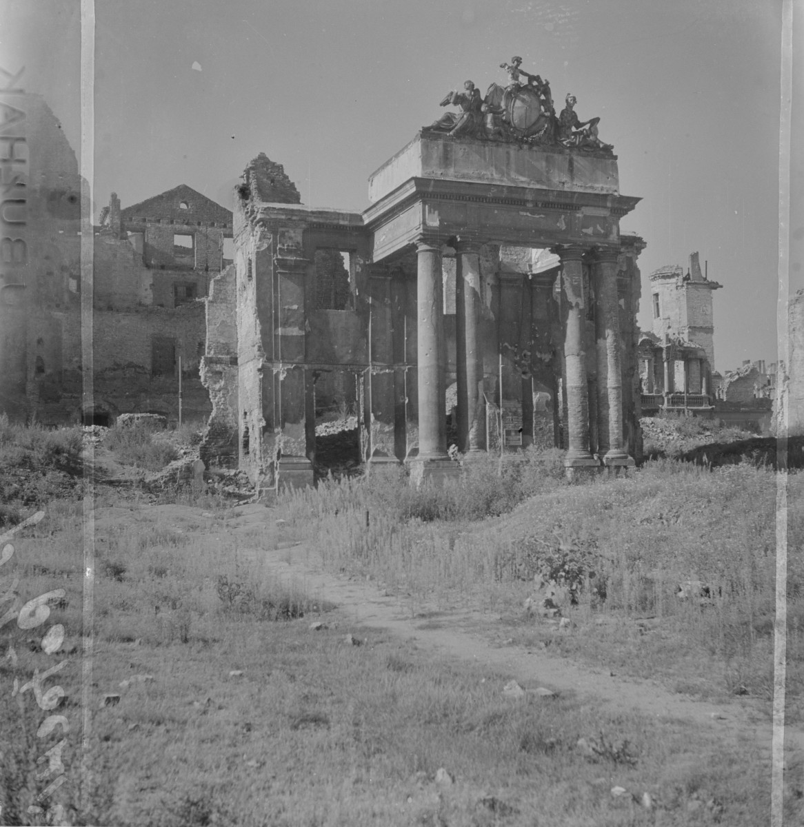 Pałac Branickich - Zachowany fragment portyku kolumnowego. Stoi jeszcze monumentalne wejście z kilkoma wysokimi, gładkimi kolumnami dźwigającymi ciężkie belkowanie. Nad nim zachowało się ozdobne zwieńczenie z rzeźbiarską dekoracją — widać kartusz i figury alegoryczne. Za portykiem i po bokach rozciągają się już właściwie tylko wypalone i poszarpane mury. Brakuje dachów, stropów i większości wnętrz, zostały jedynie fragmenty ścian z pustymi otworami okiennymi. Miejscami elewacje są oberwane aż do surowej konstrukcji., skan 1