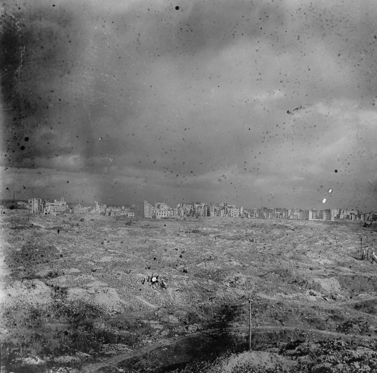 Rozległe ruiny Nalewek, sfotografowane z pewnego oddalenia, niemal panoramicznie. Na pierwszym planie rozciąga się ogromne rumowisko — nierówny teren pełen gruzu, lejów, nasypów i śladów po całkowicie zniszczonej zabudowie. Nie ma tu już ulic ani czytelnych parceli, tylko morze ruin, w którym zatarł się dawny układ miasta., skan 1