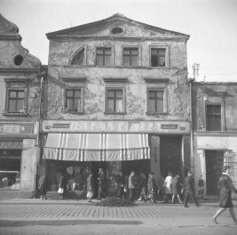 Zabudowa miejska. Elewacja frontowa kamienicy. Renesansowy szczyt. Mieszkańcy przed sklepem., skan 1
