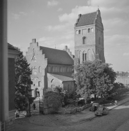 Kościół NNMP. Odbudowa. Czworoboczna wieża o prostych, niemal obronnych proporcjach. Jej elewacje są oszczędne, opracowane głównie rytmem wąskich, wysokich przeźroczy i niewielkich otworów, a całość wieńczy dach o stromym spadku, ujęty dekoracyjnymi, schodkowymi szczytami. Od strony wejścia widoczny jest schodkowy szczyt fasady, bardzo typowy dla północnoeuropejskiego i mazowieckiego gotyku ceglanego. Szczyt ten został opracowany oszczędnie, bez rozbudowanego detalu rzeźbiarskiego; jego dekoracyjność wynika przede wszystkim z samego zarysu i rytmu uskoków. Pod nim znajduje się ostrołukowy portal wejściowy. , skan 1