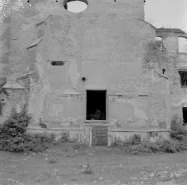 Kościół pw. Najświętszego Zbawicie Świata i MB Szkaplerznej. Ruiny od strony elewacji frontowej. Czworoboczna wieża o wyraźnie wyodrębnionych kondygnacjach. W jej górnej partii widoczne są prostokątne przeźrocza oraz zarys blankowania, co może wskazywać na historyzujące przekształcenia lub uproszczoną formę zwieńczenia. Niżej znajduje się okrągły otwór (oculus), który stanowi centralny akcent kompozycyjny elewacji., skan 1