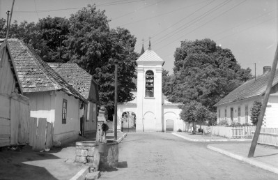 Kościół pw. św. św. Piotra i Pawła - oś widokowa w kierunku dzwonnicy z bramą. Na pierwszym planie zabudowa miejska drewnania oraz studnia miejska przy ulicy., skan 1