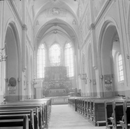 Kościół Świętej Trójcy. Wnętrze. Nawa główna prowadzi ku prezbiterium zamkniętemu wielobocznie, oświetlonemu wysokimi, ostrołukowymi oknami wypełnionymi maswerkiem. Sklepienie nawy głównej ma formę ostrołukową, z delikatnie zarysowanymi żebrami zbiegającymi się ku osi. Arkady międzynawowe są półkoliście zamknięte, o profilowanych obramieniach, co wskazuje na uproszczoną interpretację form neogotyckich z domieszką motywów historyzujących. Ściany wnętrza pokryte są dekoracją malarską – widoczne są ornamentalne bordiury, motywy roślinne oraz przedstawienia figuralne w górnych partiach ścian i w obrębie tęczy. W łuku tęczowym umieszczono symbolikę chrystologiczną – monogram IHS, a także litery Alfa i Omega, podkreślające sakralny charakter przestrzeni. Nad arkadą tęczową widoczny jest wizerunek Baranka Bożego w medalionie. , skan 1