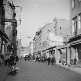 Zabudowa miejska. Oś widokowa w kierunku rynku. W oddali widoczne wieże kościoła Mariackiego. Po lewej stronie widoczny neon sklepu mięsnego., skan 1