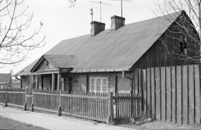 Budynek wykonany jest z bali drewnianych, prawdopodobnie w konstrukcji zrębowe. Dach dwuspadowy, o dużym nachyleniu, pokryty gontem lub papą (na zdjęciu widać raczej późniejsze pokrycie papowe, co sugeruje modernizację). W kalenicy widoczne są dwa kominy murowane z cegły. Ganek (sień frontowa) drewniany, wsparty na prostych słupach, z niewielkim trójkątnym szczytem, który dodaje budynkowi charakteru i stanowi element dekoracyjny. Ogrodzenie to drewniany płot z pionowymi sztachetami., skan 1