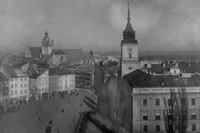 Plac Zamkowy oraz Zamek Królewski. Dwie silne dominanty: po prawej stronie wieża Zegara Zamkowego Zamku Królewskiego, a w głębi bryła i wieża kolegiaty św. Jana. Zamek Królewski widoczny jest fragmentarycznie, od strony narożnej partii z wysoką wieżą zwieńczoną smukłym hełmem. Elewacja ma charakter monumentalny, ale zarazem dość powściągliwy: prostokątne okna, wyraźny podział kondygnacji i spokojny detal podkreślają rangę budowli. Wieża zegarowa dominuje nad otoczeniem i stanowi główny akcent pionowy pierwszego planu. W głębi rozciąga się plac oraz gęsta zabudowa kamieniczna Starej Warszawy, z nieregularnym układem dachów i fasad., skan 1